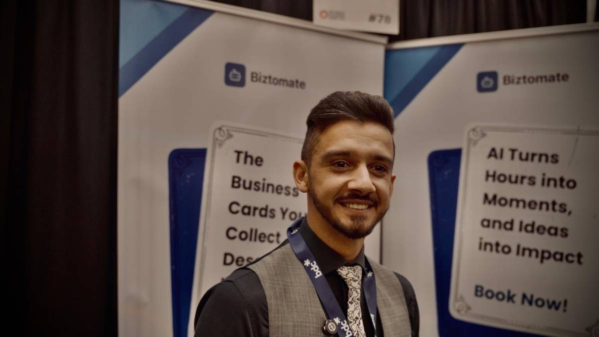 Latif Rahimi at the Biztomate booth, with banners on AI business card scanning and turning hours into impact.