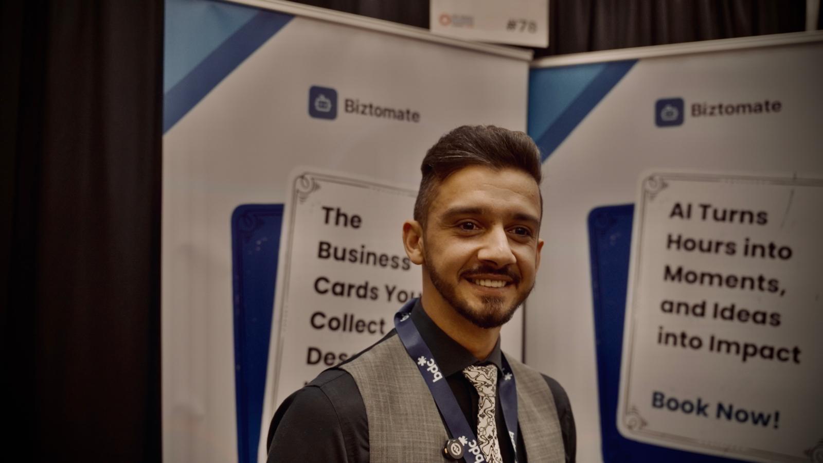 Latif Rahimi at the Biztomate booth, with banners on AI business card scanning and turning hours into impact.