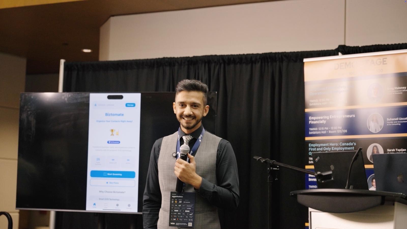 Latif Rahimi smiling on stage with the Biztomate product on the display behind him.
